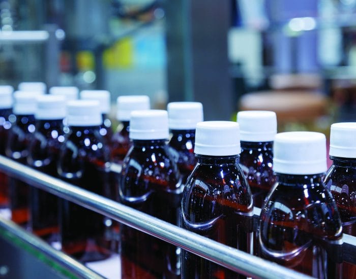 glass bottle with white cap moving on conveyor belt of auto capping and labeling machine at energy drink beverage manufacturing. pharmaceutical or beverage industry. automation technology machinery.