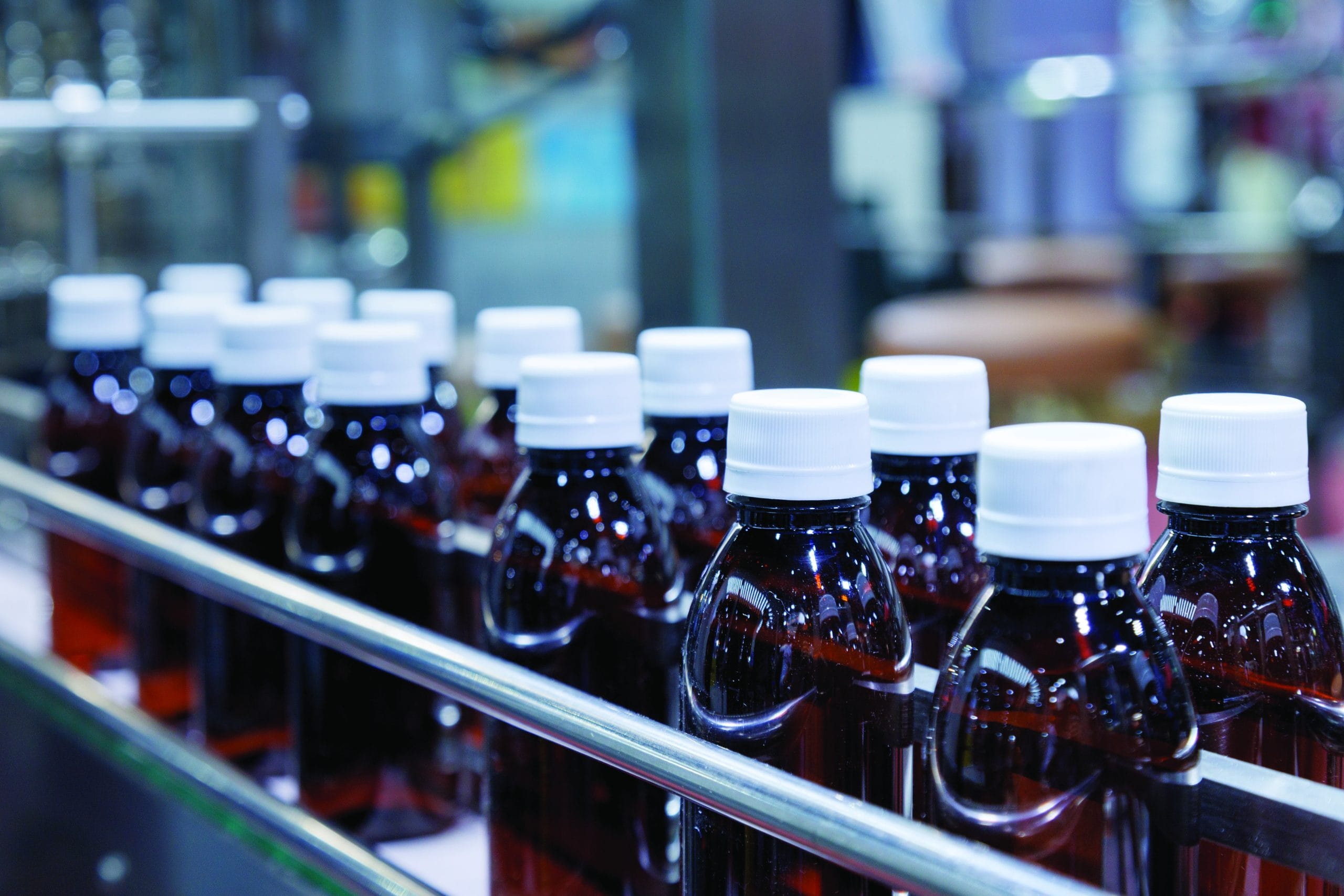 glass bottle with white cap moving on conveyor belt of auto capping and labeling machine at energy drink beverage manufacturing. pharmaceutical or beverage industry. automation technology machinery.